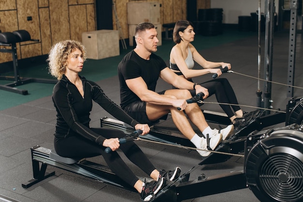 Jovem e belas mulheres malhando com máquina de remo no ginásio crossfit