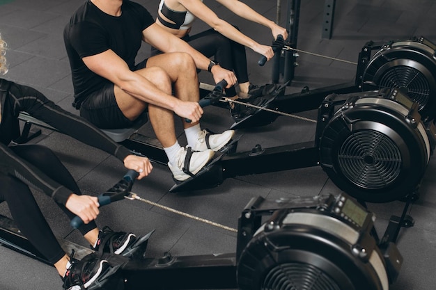 Jovem e belas mulheres malhando com máquina de remo no ginásio crossfit