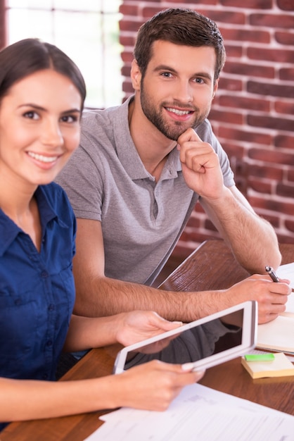 Jovem e bem-sucedido. Imagem de vista superior de um jovem alegre e uma mulher sentada no local de trabalho e sorrindo enquanto uma mulher segura o tablet digital