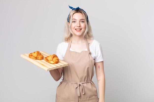 Jovem e bonita albina parecendo feliz e agradavelmente surpresa com uma bandeja de croissants