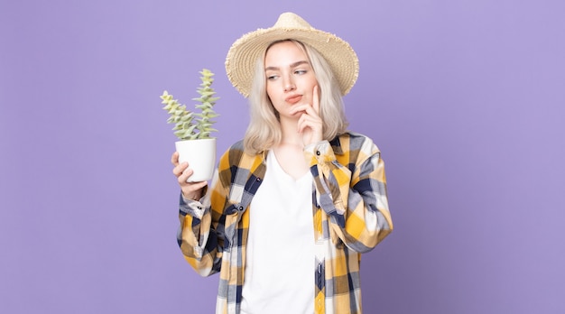 Jovem e bonita albina pensando, sentindo-se duvidosa e confusa, segurando um cacto de planta doméstica