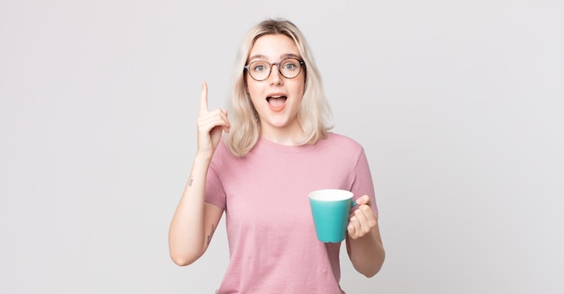 Jovem e bonita albina se sentindo um gênio feliz e animado após ter uma ideia com uma caneca de café