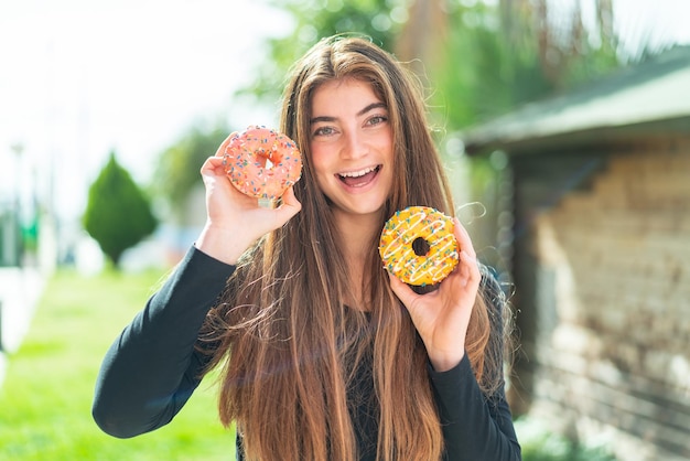 Jovem e bonita mulher caucasiana segurando donuts com expressão feliz