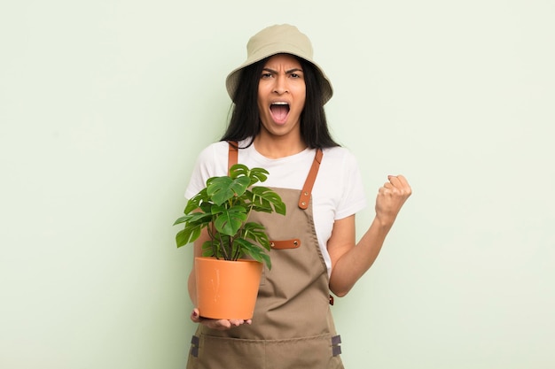Jovem e bonita mulher hispânica gritando agressivamente com um conceito de agricultor ou jardineiro de expressão de raiva