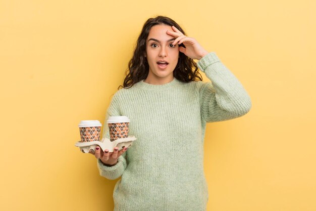 Jovem e bonita mulher hispânica olhando feliz, surpreso e surpreso, tire o conceito de café