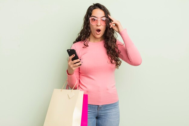 Jovem e bonita mulher hispânica parecendo surpresa ao perceber uma nova ideia de pensamento ou conceito de sacolas de compras