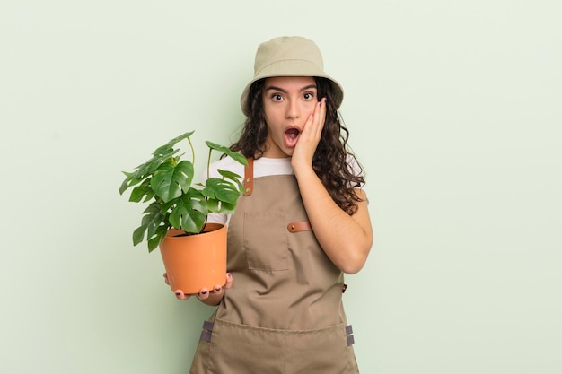 Jovem e bonita mulher hispânica se sentindo chocada e assustada com o conceito de agricultor ou jardineiro