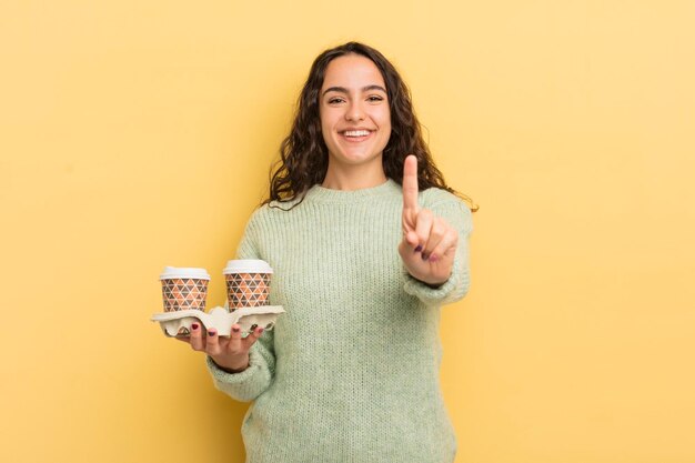 Jovem e bonita mulher hispânica sorrindo com orgulho e confiança, fazendo o conceito de café para tirar o número um