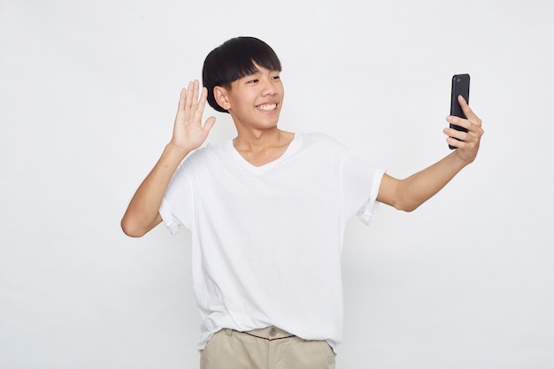 Jovem e bonito asiático mostrando um telefone para um espaço vazio na superfície branca