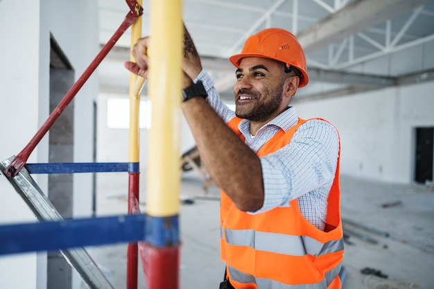 Foto jovem e bonito construtor subindo em um andaime no canteiro de obras