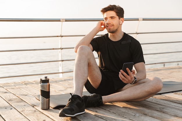 Jovem e bonito desportista sentado ao ar livre a ouvir música