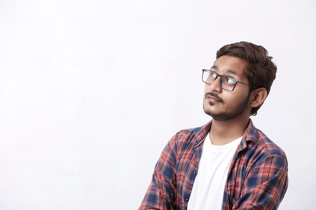 Jovem e bonito estudante universitário indiano dando expressão de pensamento no fundo branco