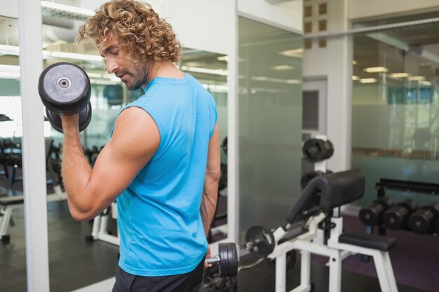 Jovem e bonito exercitando com dumbbell na academia