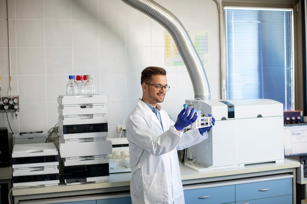 Jovem e bonito pesquisador trabalhando com amostras químicas em laboratório com sistema HPLC