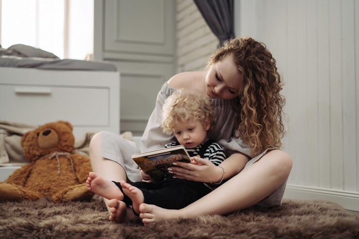Foto jovem e cacheada mãe abraçando o filho pequeno, lendo um livro juntas