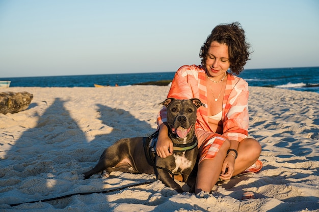 Jovem e cachorro pit bull em um momento de carinho na praia de Saquarema no Rio de Janeiro. Pôr do sol.