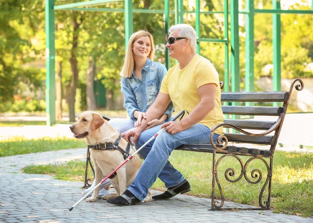 Jovem e cego com cão-guia sentado no banco no parque