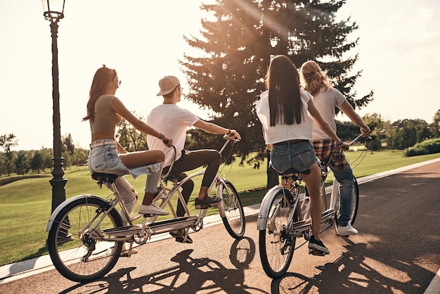 Jovem e cheio de energia. Grupo de jovens em trajes casuais pedalando juntos enquanto passam tempo despreocupados ao ar livre