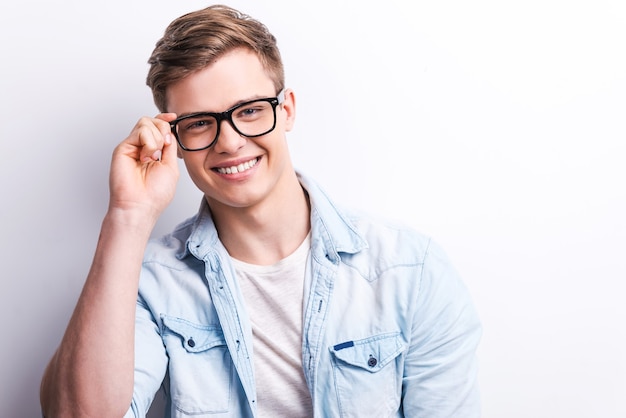 Jovem e criativo. jovem bonito ajustando seus óculos e sorrindo em pé contra um fundo cinza.