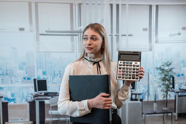 Jovem e encantadora mulher caucasiana de terno segura calculadora no trabalho de escritório de negócios