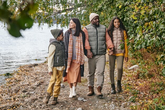 Jovem e feliz família inter-racial de pais e dois filhos caminhando ao longo da orla enquanto desfrutam de um passeio no dia de outono