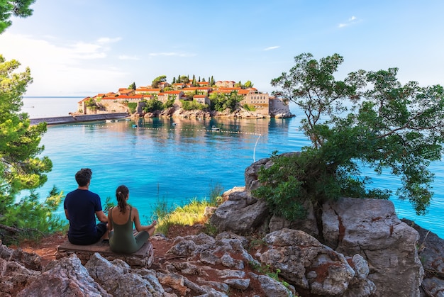 Jovem e garota meditam na rocha em frente a Sveti Stefan Islland na Riviera de Budva, Montenegro.