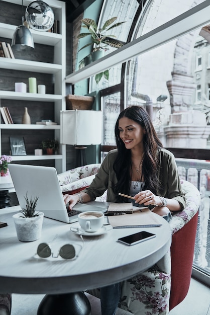 Jovem e inteligente. Mulher jovem e bonita segurando um lápis e usando o laptop