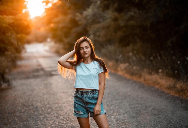 Jovem e linda adolescente morena em camiseta branca e roupas de shorts azuis posando no parque pôr do sol