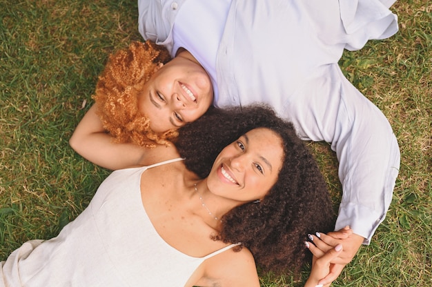 Jovem e linda feliz casal de lésbicas afro-americanas deitada na grama, rindo, estendendo as mãos