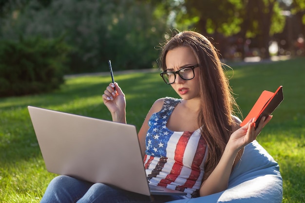 Jovem e linda garota com laptop sentado em um saco de feijão no jardim ou parque na grama verde conceito de estilo de vida moderno