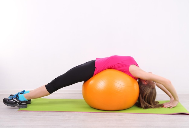 Jovem e linda garota fitness se exercitando com uma bola laranja na academia