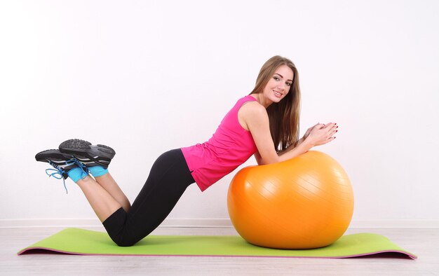 Jovem e linda garota fitness se exercitando com uma bola laranja na academia