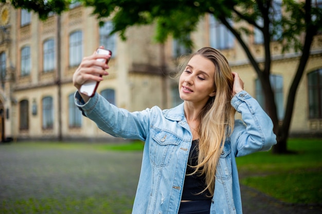 Jovem e linda garota na moda moderna com uma jaqueta jeans fazendo uma selfie ao telefone