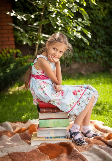 Jovem e linda garota sentada em uma grande pilha de livros no jardim