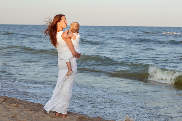 Jovem e linda mãe com uma filha pequena fica à beira-mar