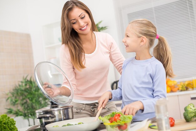 Jovem e linda mãe e sua linda filha cozinhando uma refeição saudável na cozinha.