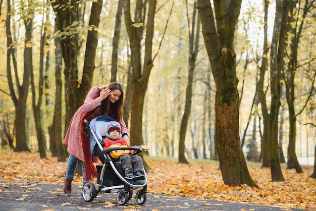 Jovem e linda mãe passa o tempo em uma caminhada com seu amado filho no parque outono.