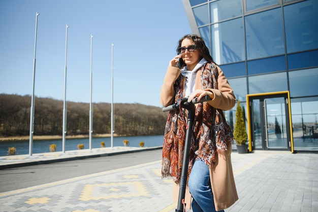 Jovem e linda mulher andando de scooter elétrica para o trabalho