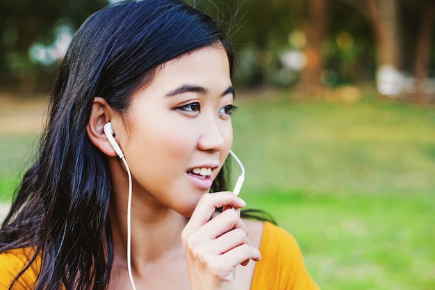 Jovem e linda mulher asiática usando fone de ouvido com mãos livres