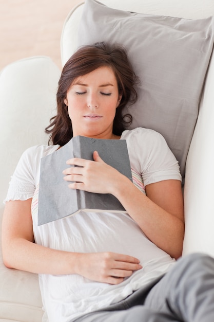 Jovem e linda mulher descansando e lendo um livro enquanto deita no sofá