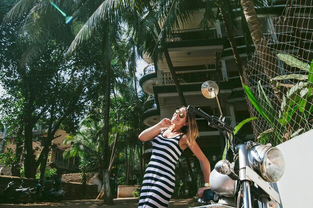 Jovem e linda mulher feliz com uma bicicleta em um vestido tropical asiático da moda de rua