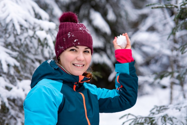 Jovem e linda mulher feliz jogando bola de neve em uma floresta de neve no inverno