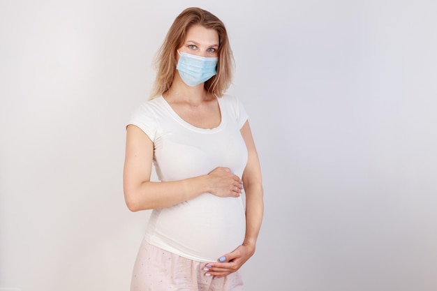 Jovem e linda mulher grávida com máscara cirúrgica médica e camiseta branca em isolamento em quarentena fica em casa