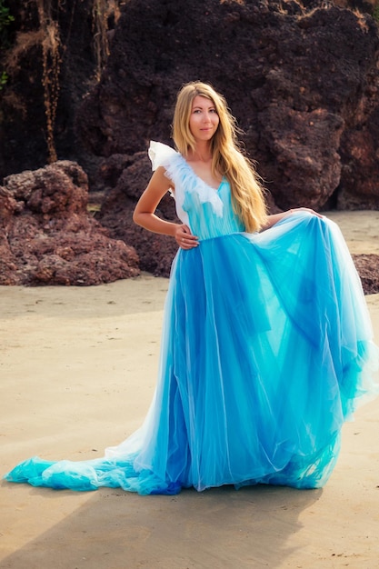 Jovem e linda mulher loira caucasiana em vestido azul longo borboleta branca na costa do mar mulher correndo em direção à liberdade oceânica