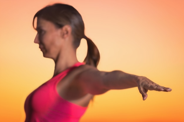 Jovem e linda mulher praticando yoga ao pôr do sol