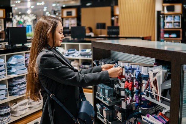 Jovem e linda mulher procurando uma gravata borboleta para presente em uma loja de supermercado