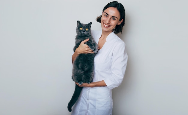 Jovem e linda mulher sorridente Veterinária segura nas mãos e examinando gato na clínica veterinária