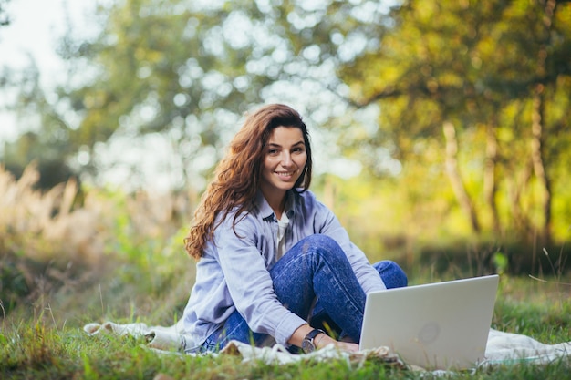 Jovem e linda mulher trabalhando em um laptop, sentada na grama