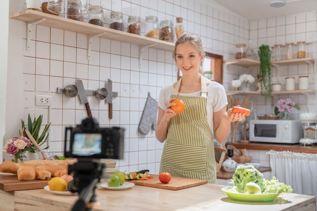 Jovem e linda mulher usando a câmera de gravação de vídeo fazer salada e confeitaria na cozinha de casa