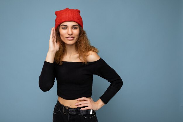 Jovem e linda mulher usando uma blusa preta cortada e um chapéu vermelho ouvindo atentamente